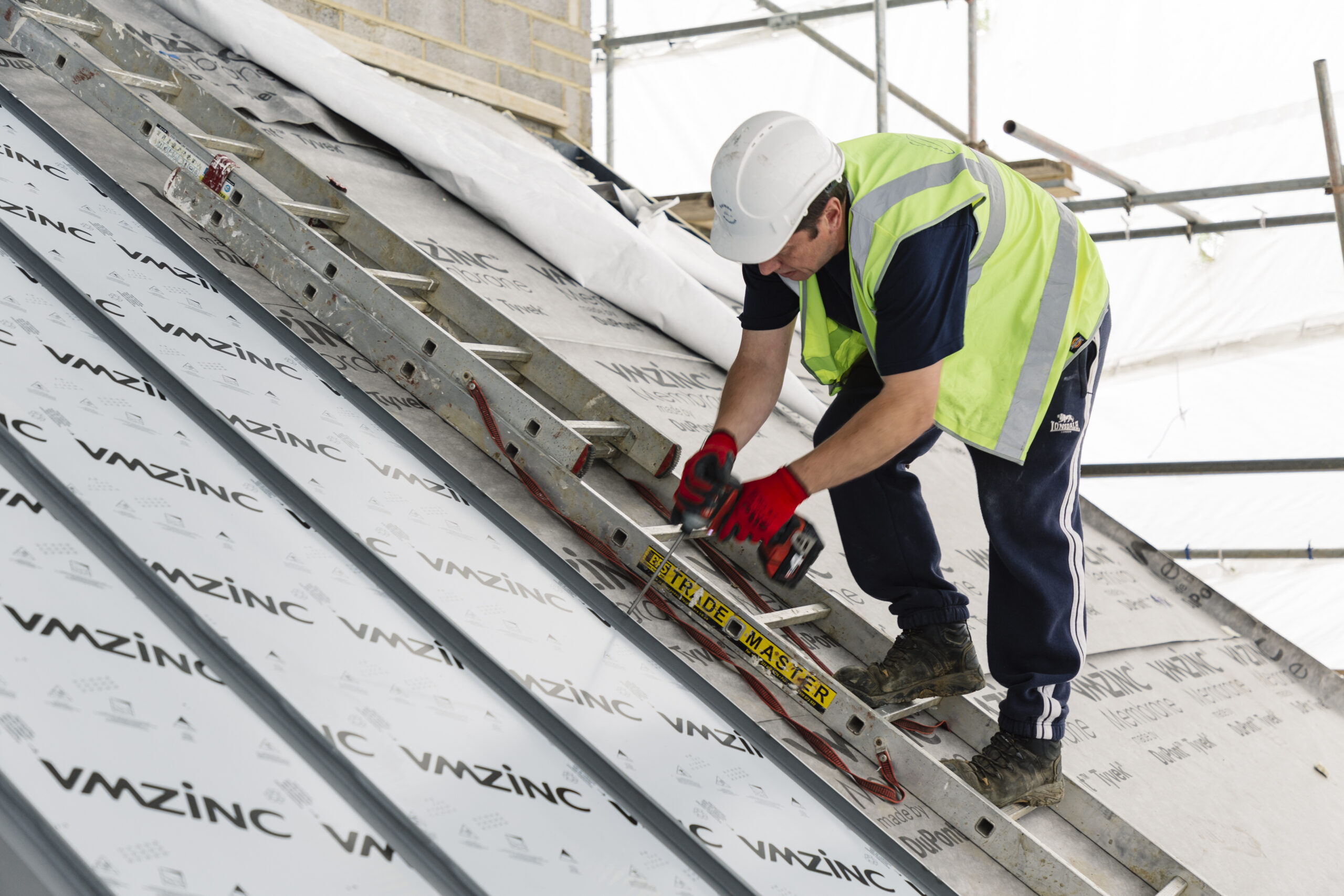 Roofer fitting standing seam panels on a roof under construction, VMZinc membrane visible